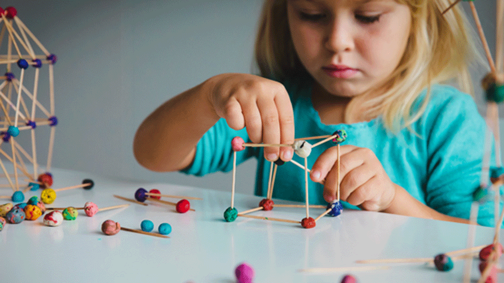 Young girl constructing things with clay and tooth sticks. 